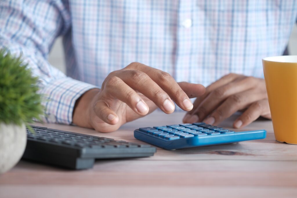Person using a calculator beside a laptop and financial records